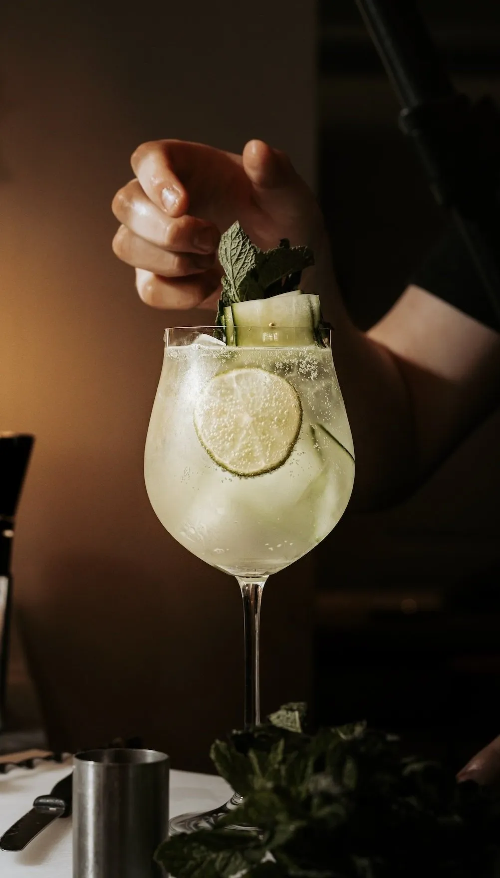 A bartender garnishing a cocktail with fresh mint and cucumber in a tall glass with lemon slices