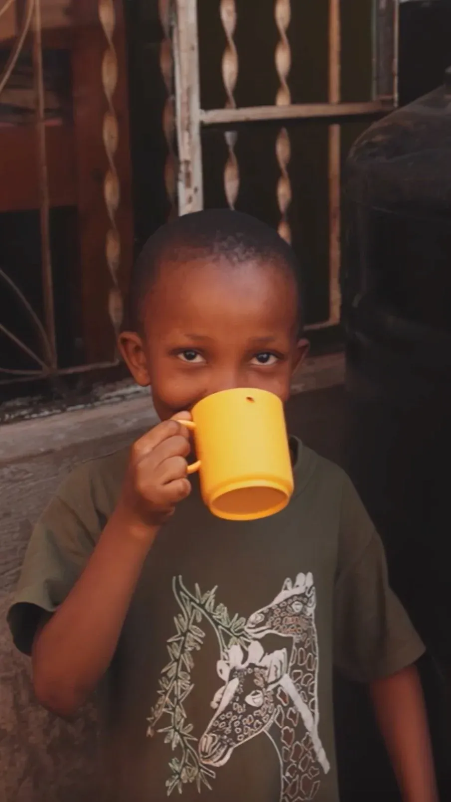A young boy with short hair drinking from a yellow mug