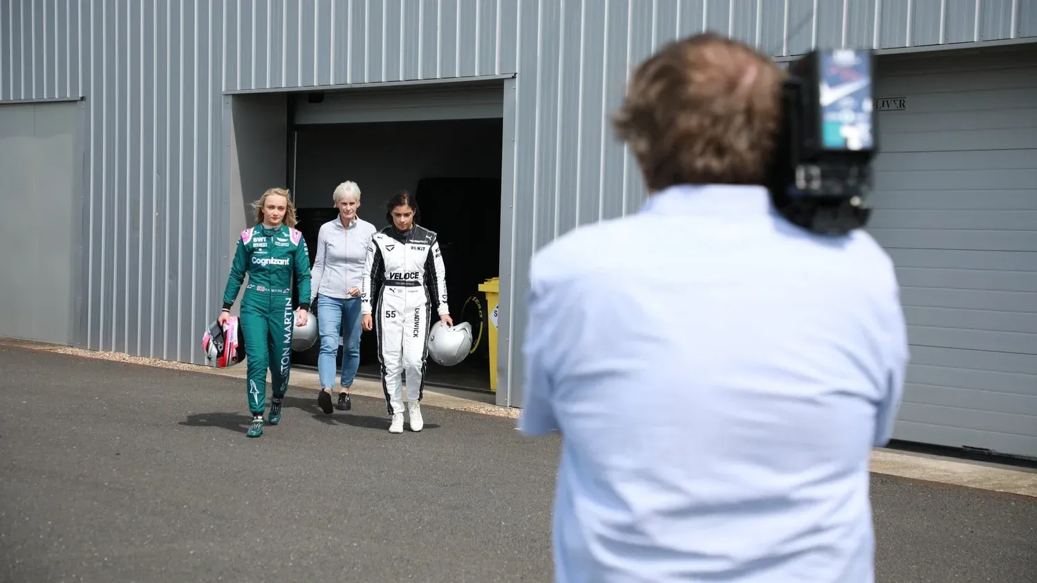 Judy Murray walking with two young racing drivers as a camera films