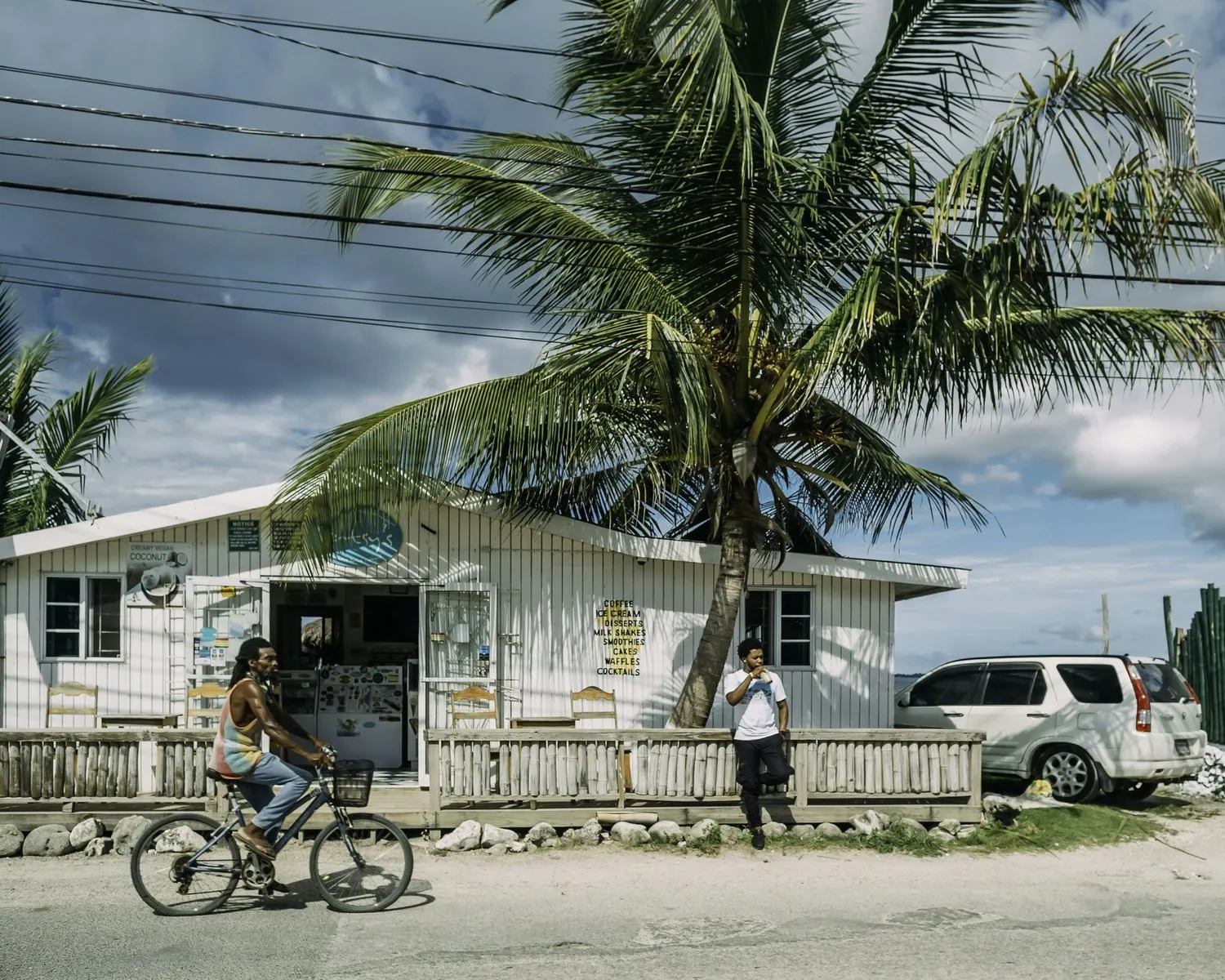 A cyclist riding past a seaside shop under palm trees in Jamaica