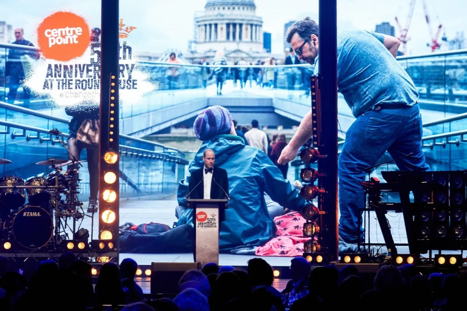 A speaker at the Centrepoint 50th anniversary event at the Roundhouse, with films on the big screen
