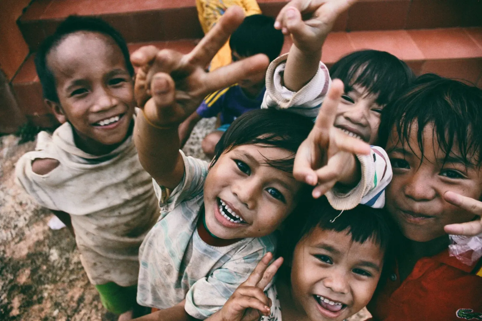 A group of smiling children making playful gestures towards the camera