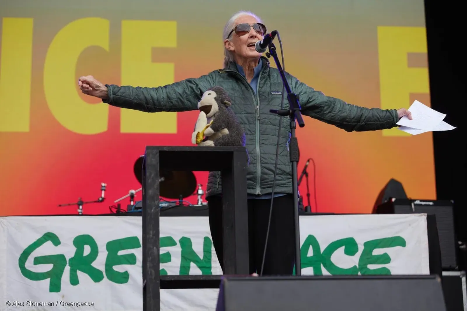 Dr Jane Goodall speaking on stage at a Greenpeace event, arms outstretched