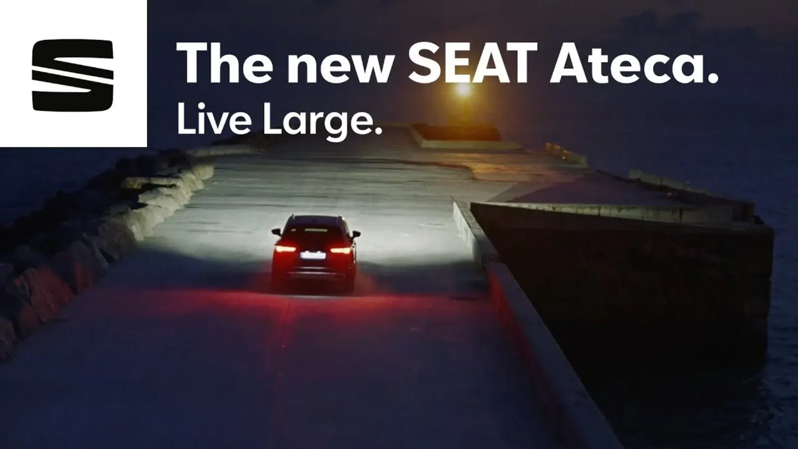 A car driving on a lit up pier at night as the sun sets over the ocean, promoting the new SEAT Ateca SUV